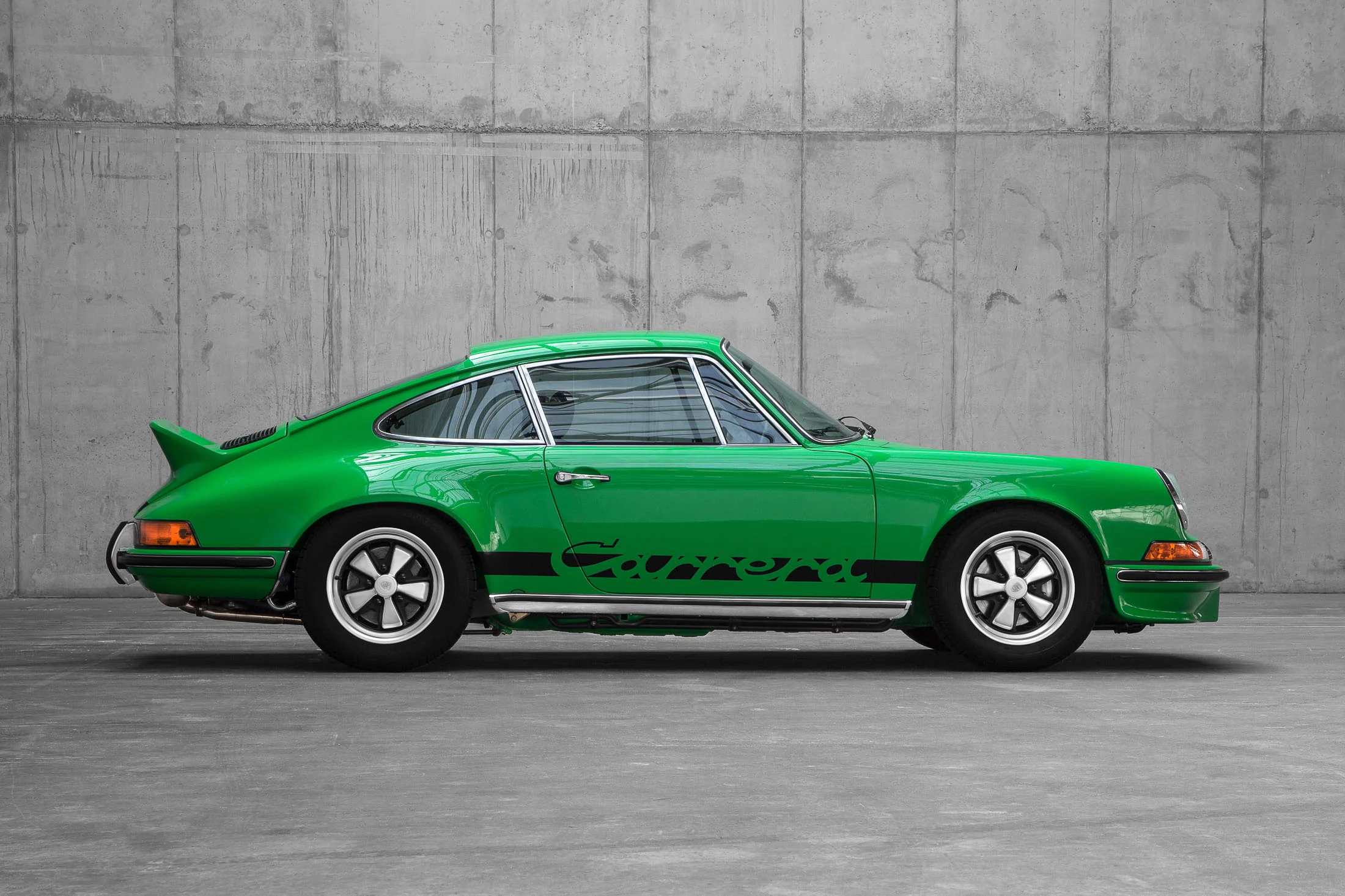 Ein klassischer grüner Sportwagen mit schwarzen Details ist im Innenbereich vor einer Betonwand geparkt.